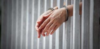handcuffed hands resting through prison bars