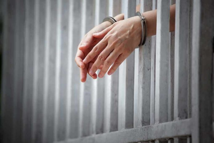shutterstock_1018630735 handcuffed hands resting through prison bars