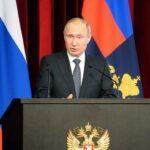 Vladimir Putin speaking at a podium with microphones