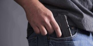 Hand placing a handgun into a jeans pocket