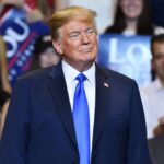 Donald Trump at a rally wearing a dark suit and blue tie