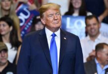 Donald Trump at a rally wearing a dark suit and blue tie