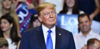 Donald Trump at a rally wearing a dark suit and blue tie