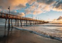 Boardwalk Shredded – Worse Hits Next Week Wooden pier stretching over ocean waves at sunset