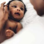 Baby lying on a bed looking up at an adult