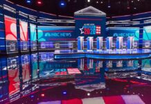 Televised debate stage with multiple podiums and bright red, white, and blue lighting
