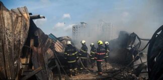 Firefighters amid twisted metal and smoke at a disaster site