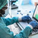 Critical Delay Exposed — Virus Gains Ground Healthcare worker in PPE using a laptop in a lab