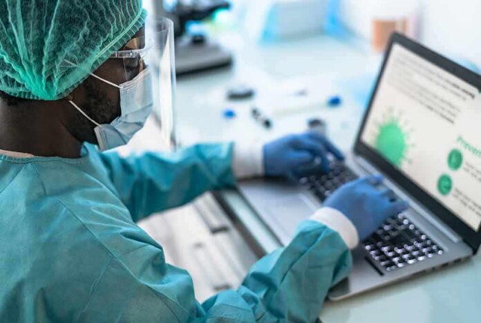 shutterstock_1899363976 Healthcare worker in PPE using a laptop in a lab