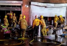 Encampment Infernos Overwhelm LA Firefighters work outside a damaged warehouse with debris and hoses