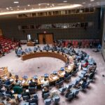 Delegates seated around a circular conference table in a large chamber