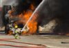 Firefighter spraying water on a vehicle engulfed in flames
