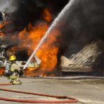 Firefighter spraying water on a vehicle engulfed in flames