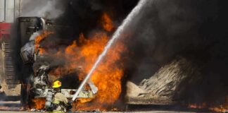 Firefighter spraying water on a vehicle engulfed in flames