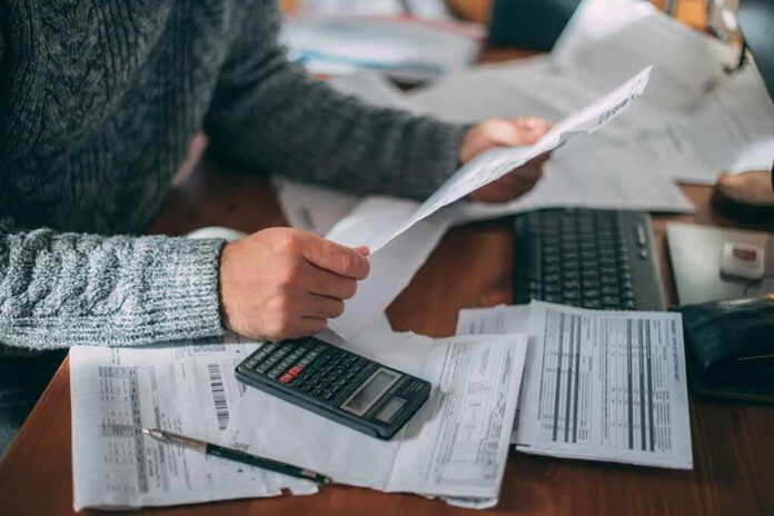 shutterstock_2232534015 Person reviewing bills with calculator at cluttered desk
