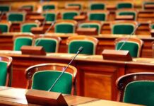 Empty legislative chamber with green upholstered chairs and wooden desks