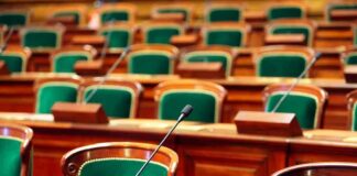 Empty legislative chamber with green upholstered chairs and wooden desks