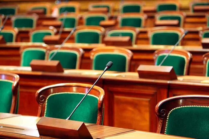 Empty legislative chamber with green upholstered chairs and wooden desks