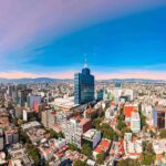 City skyline with tall blue-glass tower at center under clear sky
