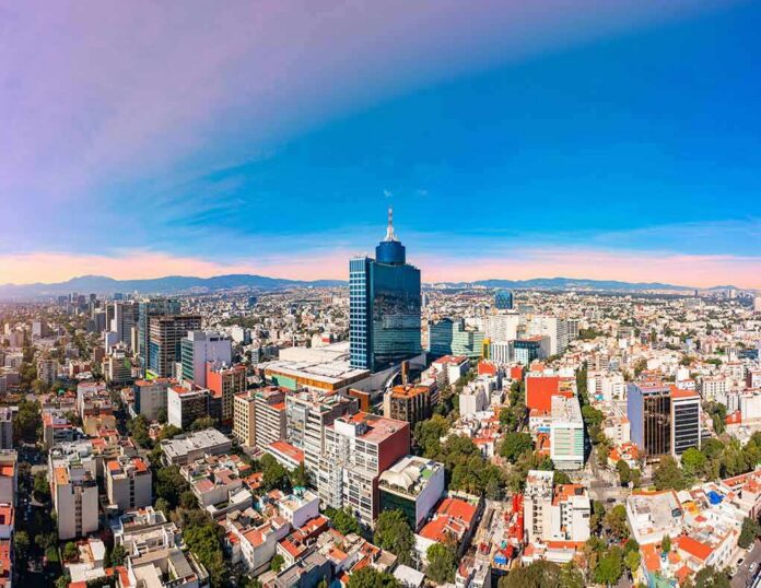 shutterstock_2271838321 City skyline with tall blue-glass tower at center under clear sky
