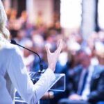 Speaker at podium addressing a blurred audience