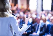 Communism Creep? Defector Sounds Alarm Speaker at podium addressing a blurred audience