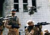 Quadcopter drone flying above soldiers in camouflage