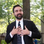man in a suit speaking outdoors with hands on chest