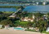 Aerial view of a waterfront estate with pool, lawns, and palm trees
