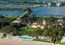 Aerial view of a waterfront estate with pool, lawns, and palm trees