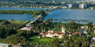 Aerial view of a waterfront estate with pool, lawns, and palm trees