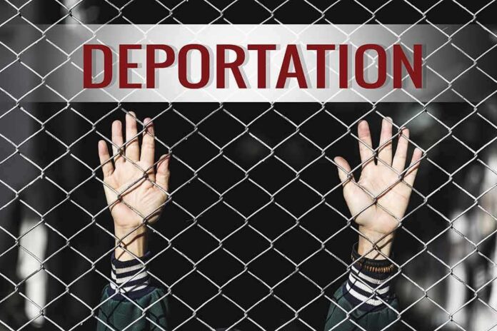 Hands gripping chain-link fence with deportation sign