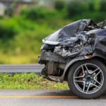 Crashed black car with severe front-end damage on roadside