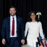 Near-Fall Fury: Protocol Or Failure? Two people holding hands on stage with U.S. flags behind them