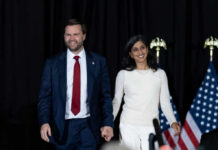 Near-Fall Fury: Protocol Or Failure? Two people holding hands on stage with U.S. flags behind them