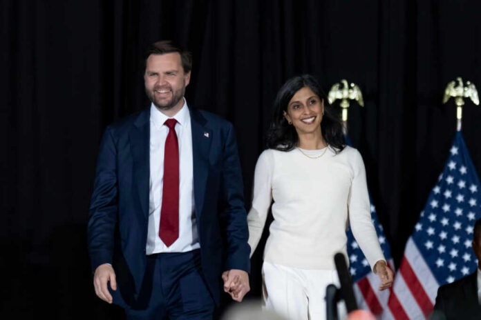54801cb8-0515-4c34-a2d8-f79705e6683e_shutterstock2542633801jpg.jpeg Two people holding hands on stage with U.S. flags behind them