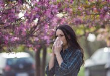 Early Wave Warning: Shot Now, Not Later Woman sneezing into tissue under blooming pink trees