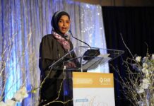 Minnesota Fraud Cloud Hangs Over Omar Ilhan Omar speaking at a podium on a decorated stage