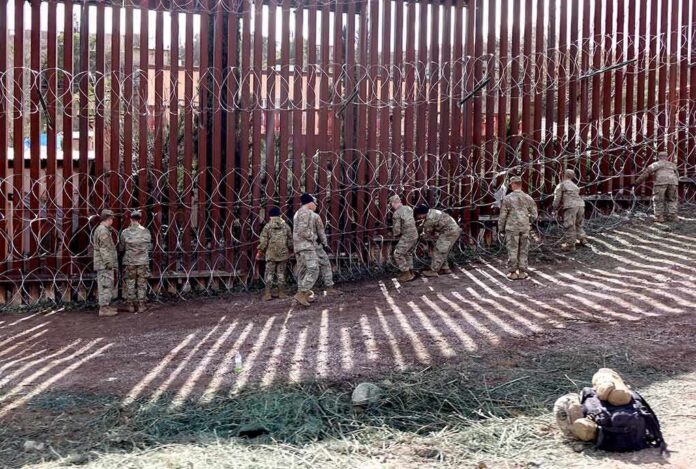 Soldiers install concertina wire along a tall border fence