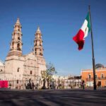 Mexican flag waving in a plaza with a historic cathedral