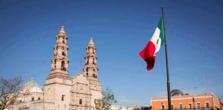 Mexican flag waving in a plaza with a historic cathedral