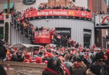 One Shoulder Tap Sparks a Sideline Firestorm Christian Jones and Teddy Williams in a large outdoor crowd at a Kansas City football rally