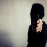 person in a hoodie pointing a handgun toward the camera