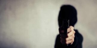 person in a hoodie pointing a handgun toward the camera