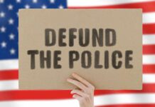 Hand holding protest sign against blurred American flag
