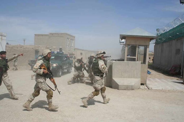 Soldiers in desert uniforms run past a checkpoint amid dust