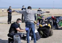 Police officers process group of people on a beachside pavement