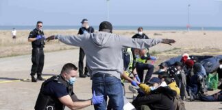 Police officers process group of people on a beachside pavement