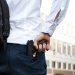 person holding a handgun behind their back near a building