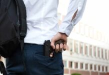 person holding a handgun behind their back near a building